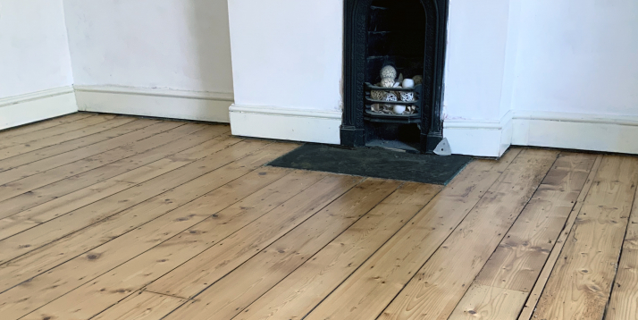 Freshly sanded and finished floorboards in white room with fireplace